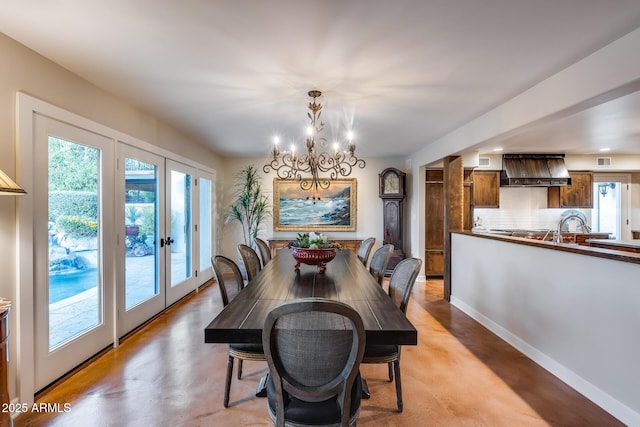 dining area with healthy amount of natural light, finished concrete flooring, a chandelier, and french doors