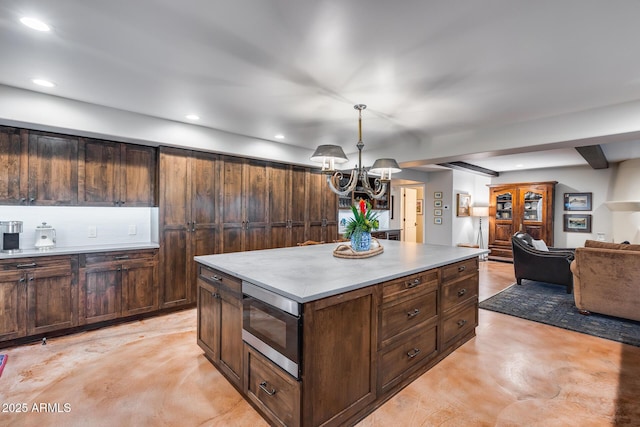 kitchen featuring stainless steel microwave, finished concrete flooring, a chandelier, open floor plan, and a kitchen island