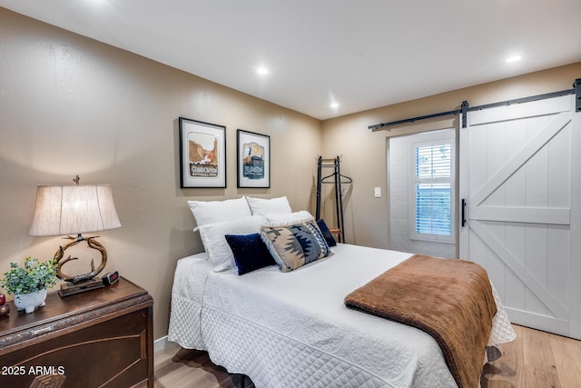 bedroom with wood finished floors, a barn door, recessed lighting, and baseboards