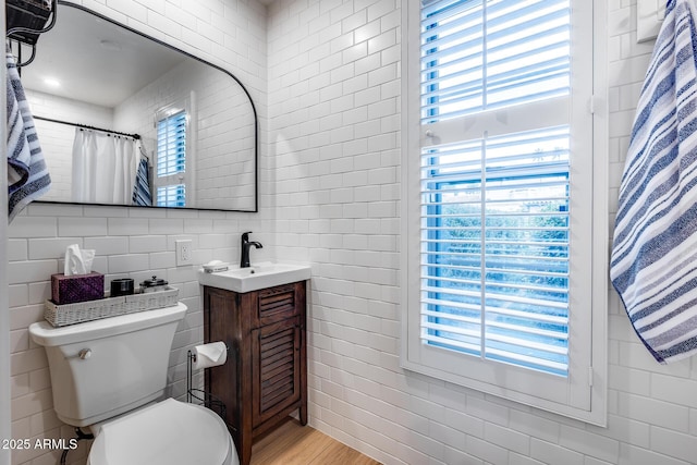 full bathroom with tile walls, healthy amount of natural light, vanity, and toilet
