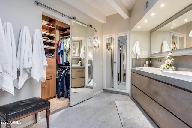bathroom featuring beam ceiling, recessed lighting, double vanity, a spacious closet, and tasteful backsplash