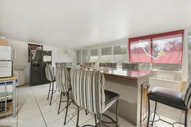 kitchen featuring light tile patterned flooring, a breakfast bar, and black refrigerator with ice dispenser