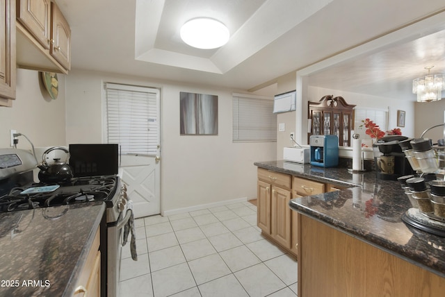 kitchen featuring stainless steel range with gas cooktop, dark stone countertops, light tile patterned floors, a raised ceiling, and an inviting chandelier