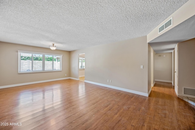 empty room with a textured ceiling, wood finished floors, and baseboards