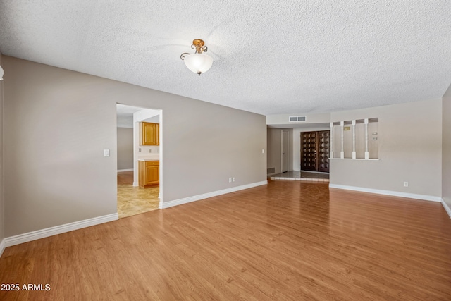 unfurnished living room with light wood-style flooring, a textured ceiling, and baseboards