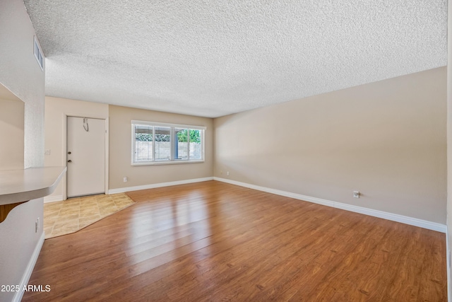 unfurnished living room featuring wood finished floors, a textured ceiling, and baseboards