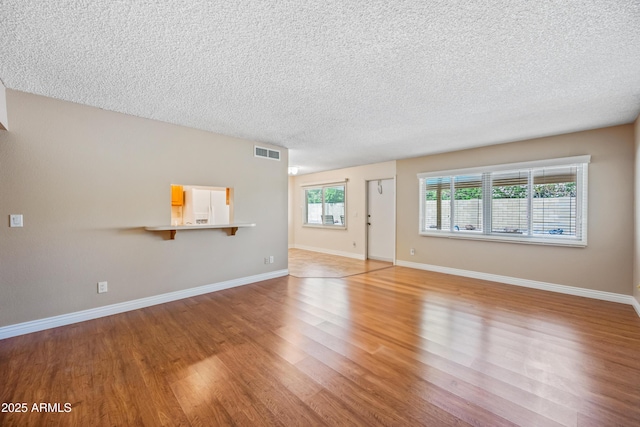 unfurnished living room with light wood-type flooring, a textured ceiling, and baseboards