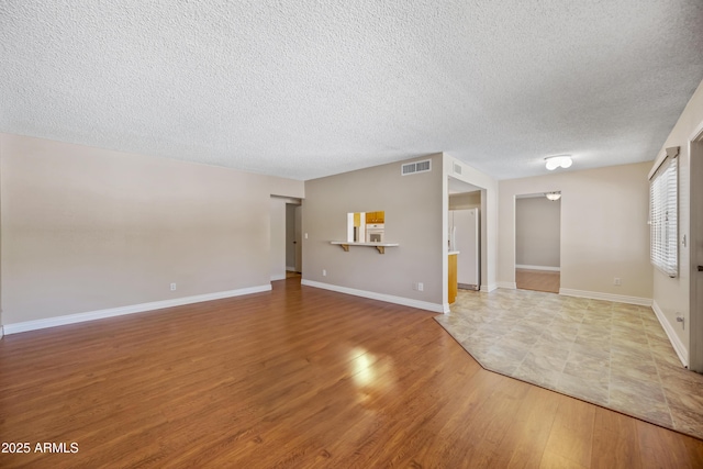 empty room with wood finished floors, a textured ceiling, and baseboards