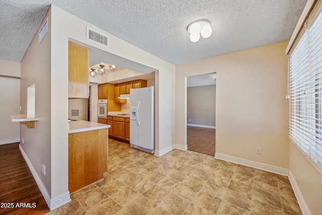 kitchen with white appliances, a textured ceiling, brown cabinetry, light countertops, and baseboards