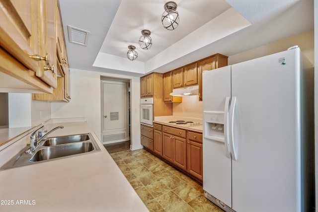 kitchen with white appliances, a tray ceiling, a sink, light countertops, and under cabinet range hood