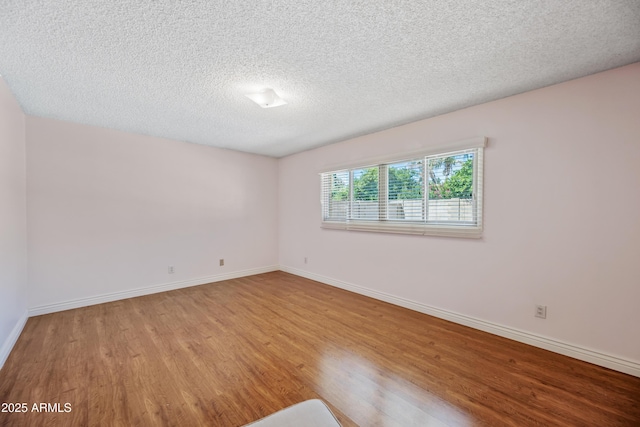 empty room featuring wood finished floors, a textured ceiling, and baseboards