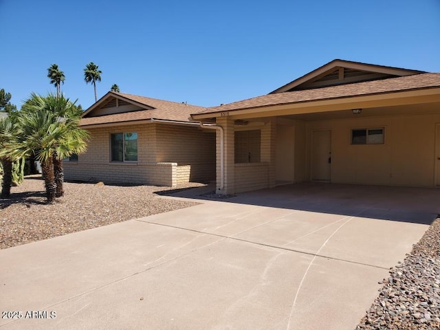ranch-style home featuring driveway, roof with shingles, and brick siding