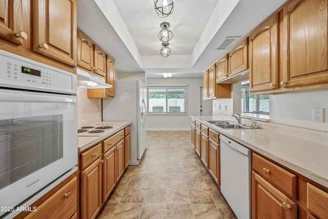 kitchen featuring white appliances, a sink, under cabinet range hood, light countertops, and a raised ceiling