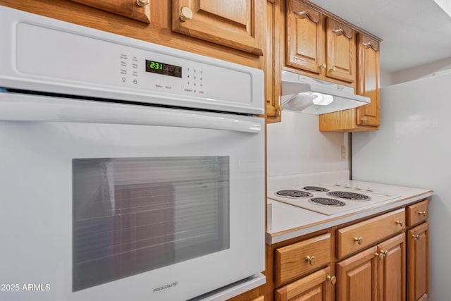 kitchen with under cabinet range hood, white appliances, light countertops, and brown cabinetry