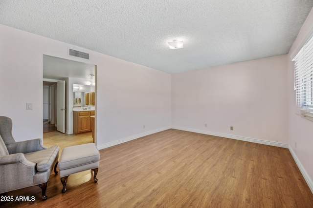 unfurnished room with light wood-style flooring, a textured ceiling, and baseboards