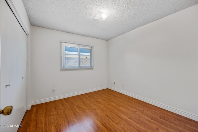 spare room with a textured ceiling, wood finished floors, and baseboards