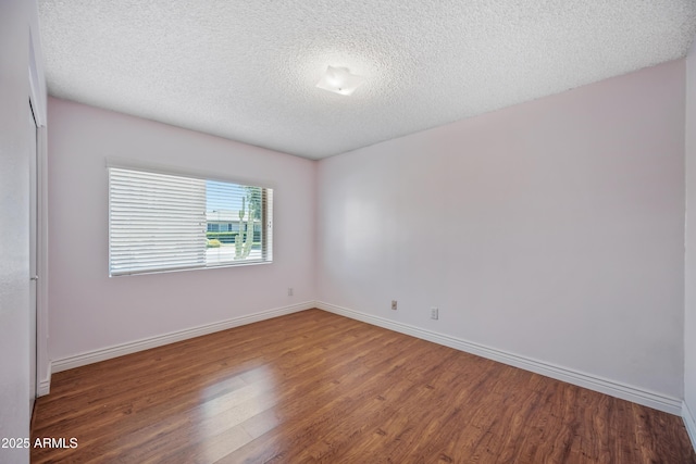 spare room with wood finished floors, baseboards, and a textured ceiling