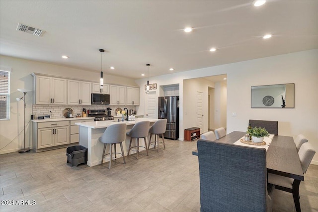 kitchen with a center island with sink, a kitchen breakfast bar, pendant lighting, stainless steel appliances, and backsplash