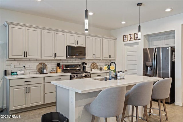 kitchen with appliances with stainless steel finishes, backsplash, a kitchen island with sink, and light tile patterned floors