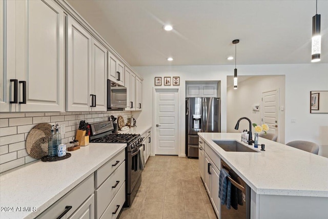 kitchen featuring stainless steel appliances, a kitchen island with sink, sink, backsplash, and decorative light fixtures