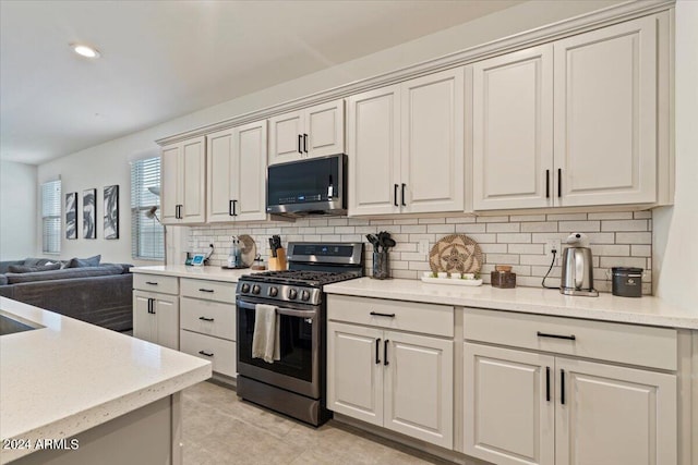 kitchen with appliances with stainless steel finishes, tasteful backsplash, light stone counters, and light tile patterned floors