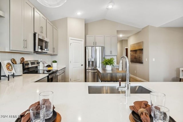 kitchen featuring lofted ceiling, a sink, stainless steel appliances, light countertops, and backsplash