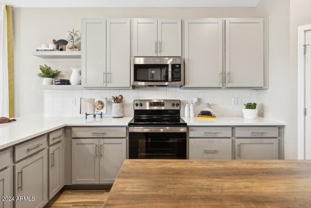 kitchen featuring decorative backsplash, gray cabinets, stainless steel appliances, and open shelves