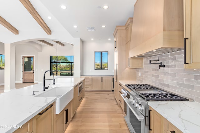 kitchen featuring beam ceiling, light stone countertops, appliances with stainless steel finishes, and premium range hood