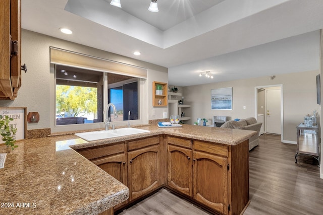 kitchen featuring brown cabinets, a peninsula, light countertops, light wood-type flooring, and a sink