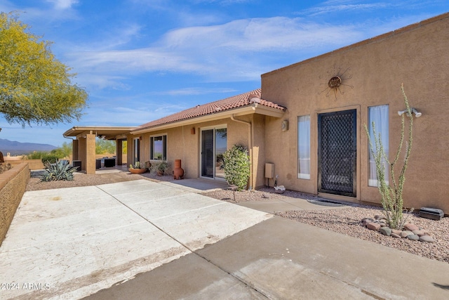 view of exterior entry featuring a tile roof, a patio, and stucco siding