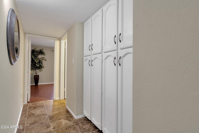 hallway featuring a textured wall and baseboards