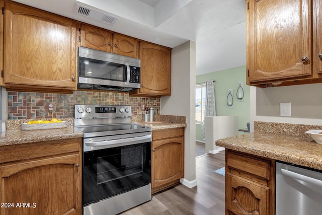 kitchen featuring visible vents, decorative backsplash, brown cabinetry, dark wood-style floors, and stainless steel appliances