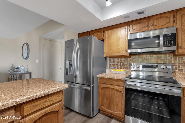 kitchen with brown cabinets, visible vents, backsplash, appliances with stainless steel finishes, and light wood-style floors