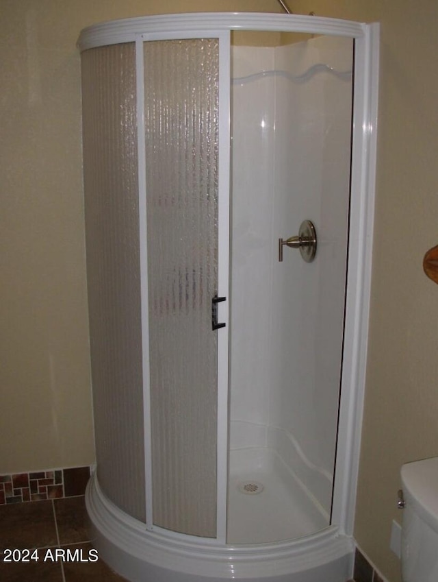 bathroom featuring tile patterned flooring, a shower stall, toilet, and baseboards