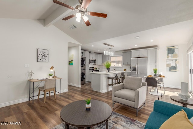 living room with ceiling fan, lofted ceiling with beams, dark wood-type flooring, stacked washing maching and dryer, and sink