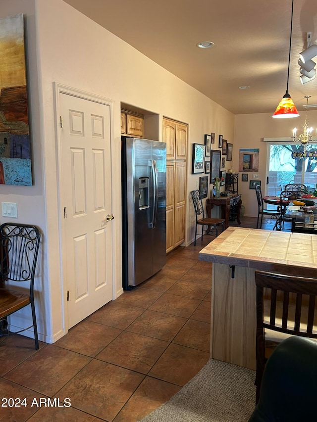 kitchen with dark tile patterned floors, an inviting chandelier, tile countertops, hanging light fixtures, and stainless steel fridge with ice dispenser