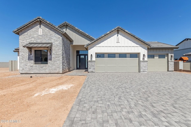 view of front of house featuring an attached garage, stone siding, board and batten siding, and decorative driveway