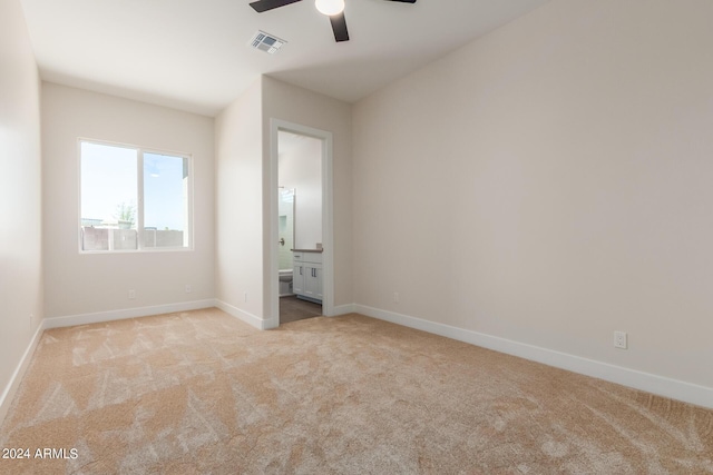 unfurnished bedroom featuring ceiling fan, ensuite bathroom, light carpet, visible vents, and baseboards