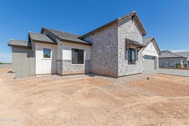 back of property featuring a garage, stone siding, and board and batten siding