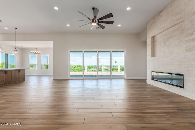 unfurnished living room featuring a fireplace, recessed lighting, light wood-style floors, baseboards, and ceiling fan with notable chandelier