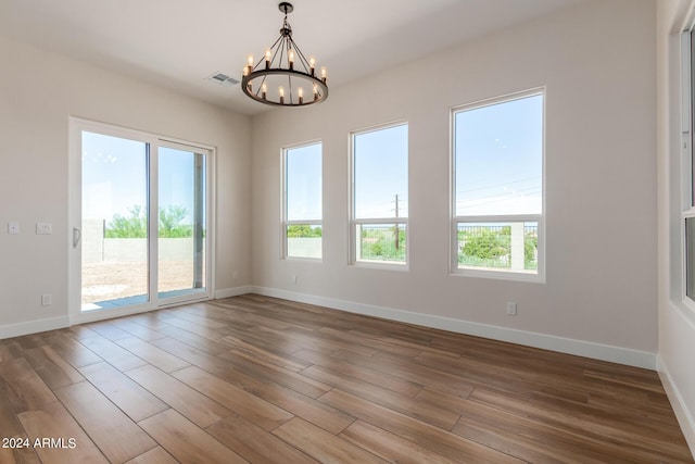 empty room featuring wood finished floors, visible vents, baseboards, and an inviting chandelier