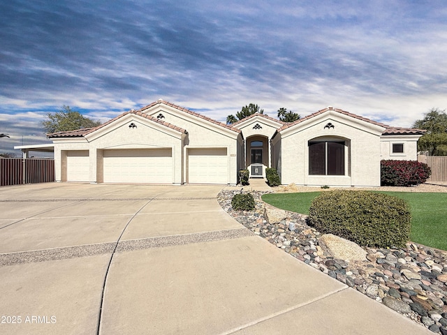 mediterranean / spanish home with an attached garage, fence, driveway, and stucco siding