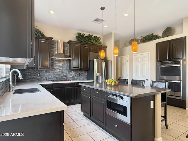 kitchen featuring a breakfast bar area, visible vents, a sink, appliances with stainless steel finishes, and wall chimney exhaust hood