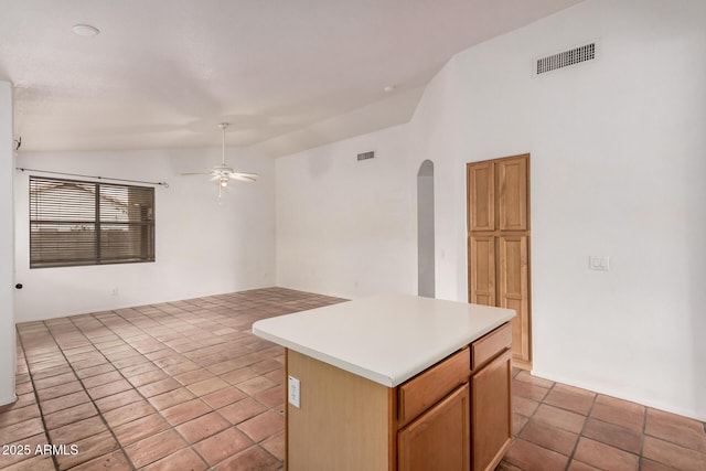 kitchen featuring a ceiling fan, visible vents, lofted ceiling, arched walkways, and a center island