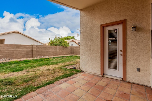 view of exterior entry with a patio, fence, and stucco siding