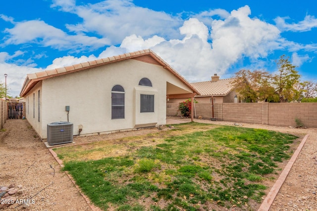 back of property featuring a tile roof, central AC unit, stucco siding, a chimney, and a fenced backyard