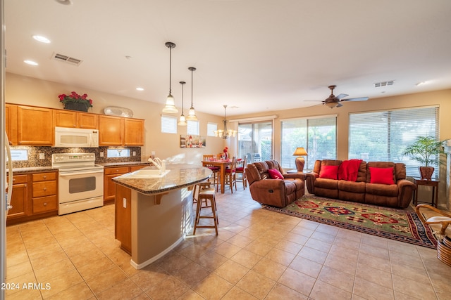 kitchen featuring decorative light fixtures, ceiling fan with notable chandelier, white appliances, a breakfast bar, and light stone counters