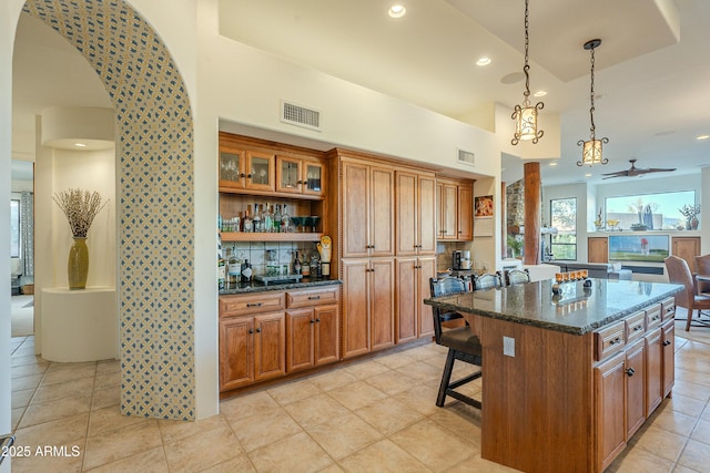 kitchen with decorative light fixtures, dark stone countertops, a kitchen breakfast bar, a kitchen island, and a high ceiling