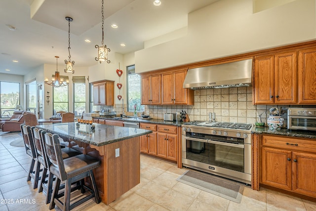 kitchen with wall chimney range hood, a breakfast bar, appliances with stainless steel finishes, dark stone countertops, and a kitchen island