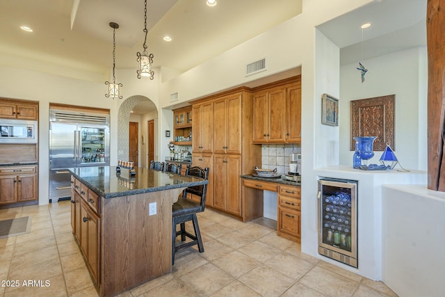 kitchen with a kitchen island, beverage cooler, a kitchen breakfast bar, dark stone counters, and built in appliances